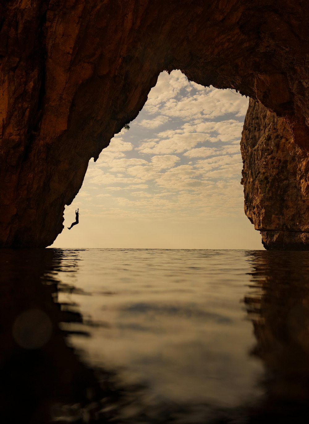 a person standing in the water in front of a cave