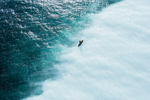 Aerial shot of a surfer riding a wave at sunrise on a beach in Região dos Lagos.