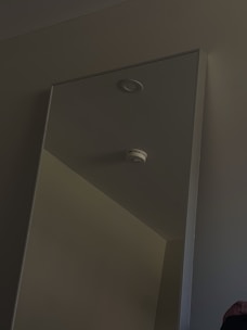 Smoke detector mounted on a ceiling in a bright room.