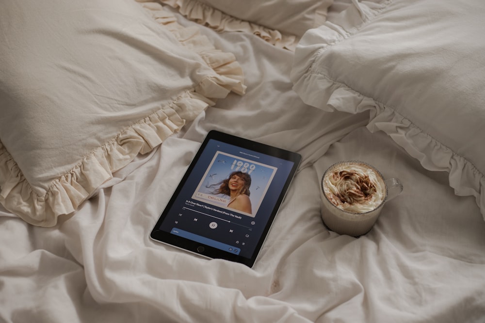 a tablet sitting on a bed next to a cup of coffee