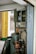 An interior wall features an old electrical panel with several open compartments. Surrounding the panel are multiple electrical sockets and a variety of cords. Below the panel, a red and black industrial drill press is positioned. The area is filled with miscellaneous tools and metal panels, suggesting a functioning workspace. The wall is tiled and adorned with small decorative items, including a strip of red paper with gold lettering.