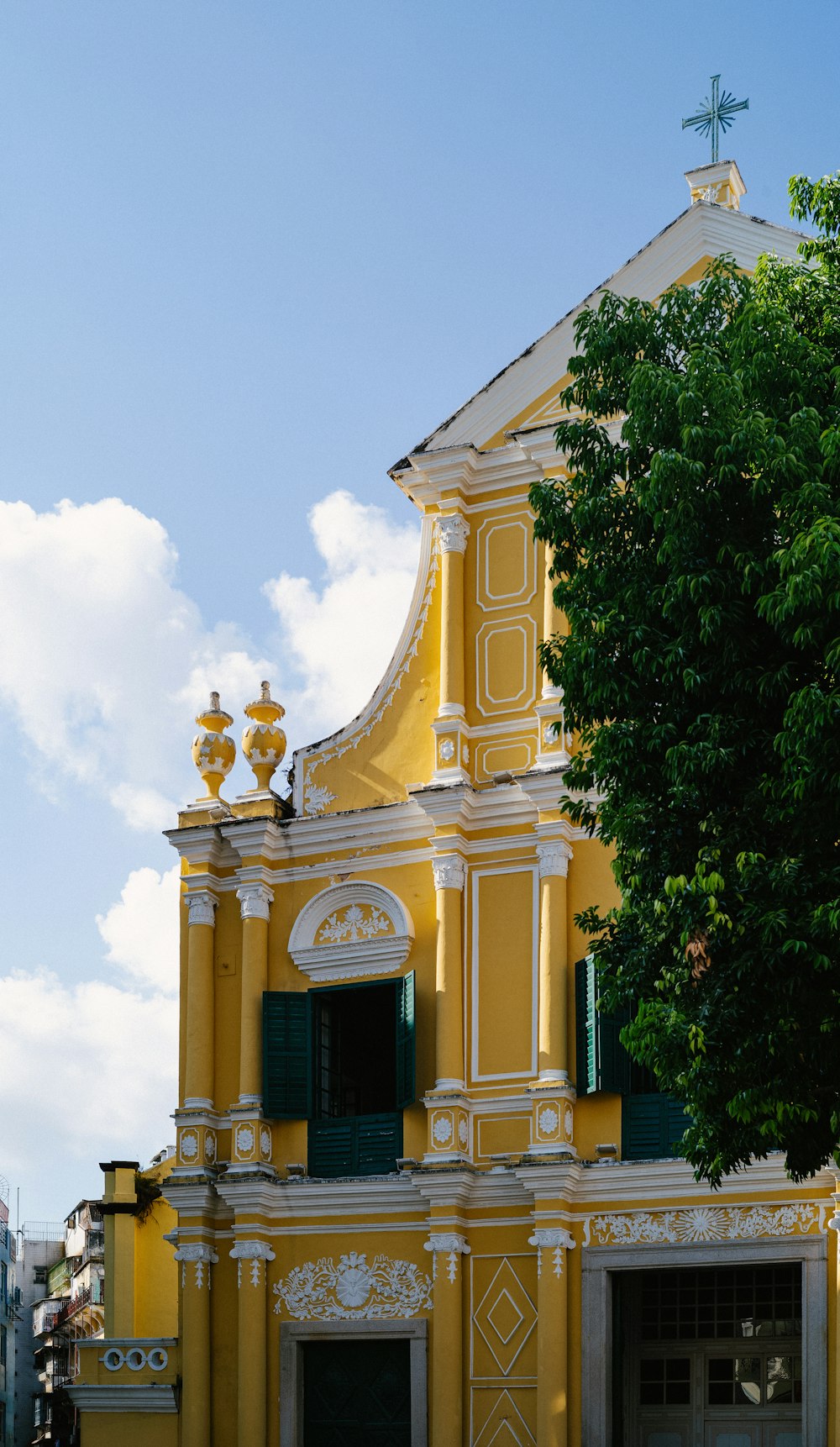 a yellow building with green shutters and a cross on top