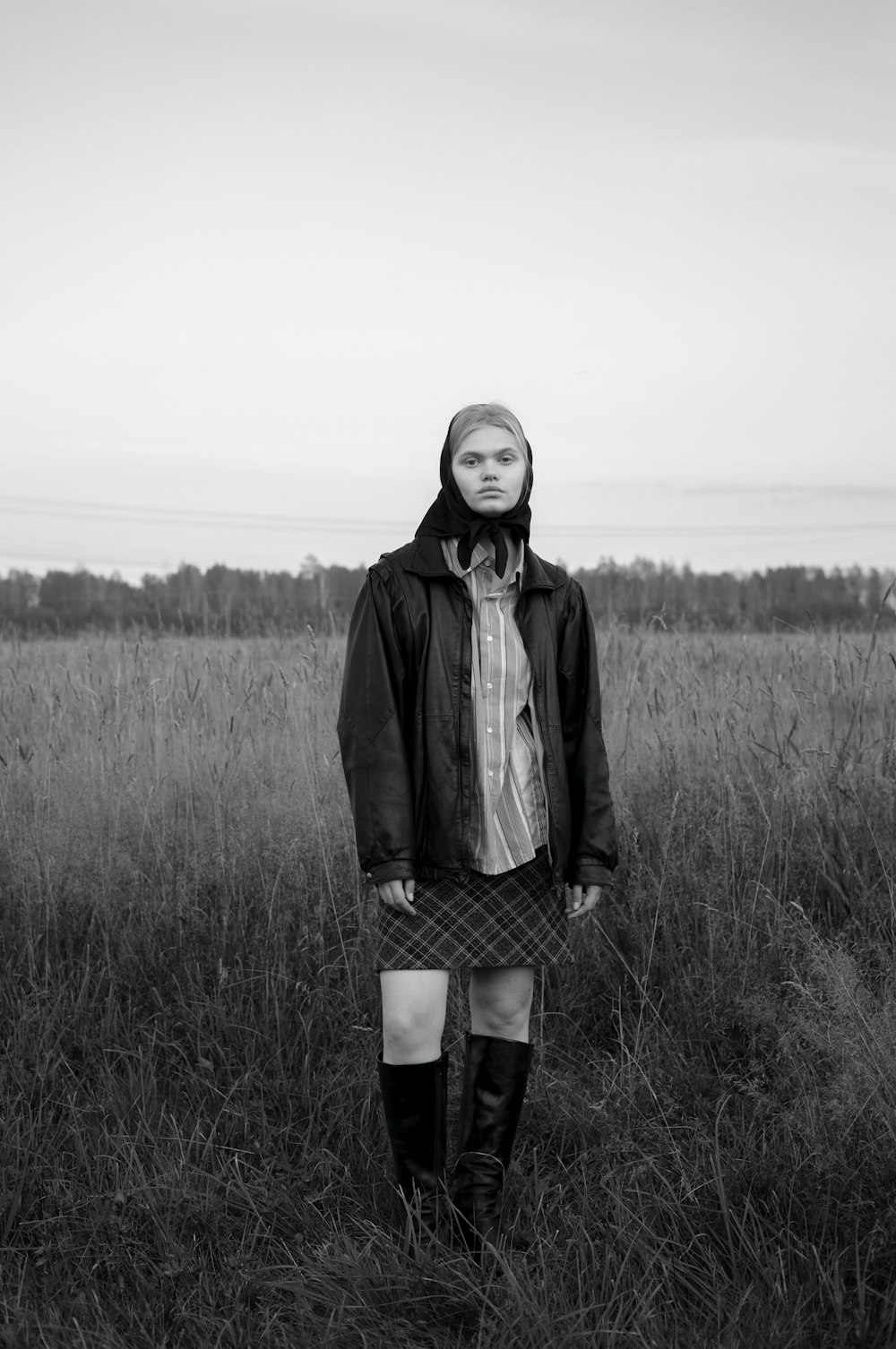 a woman standing in a field wearing a skirt and boots