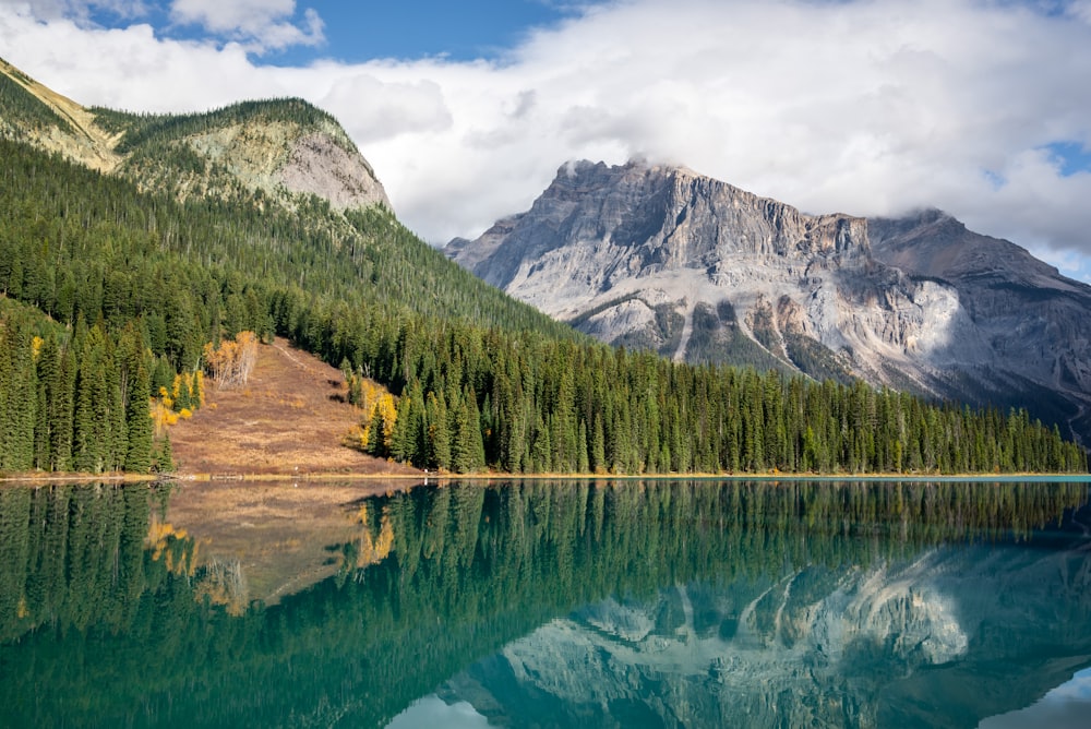 a lake surrounded by trees and mountains under a cloudy sky