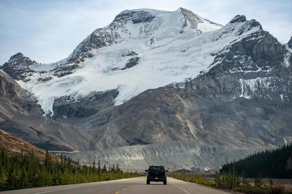 a car driving down a road in front of a snow covered mountain