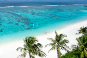 A serene tropical beach at sunset with calm turquoise waters and a couple walking hand in hand along the shore.