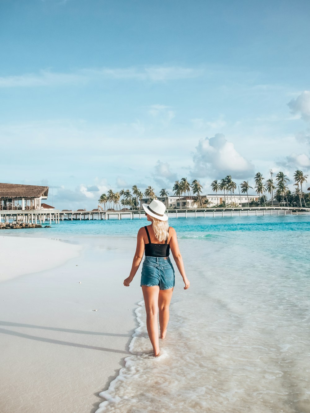 a woman walking on the beach with a hat on