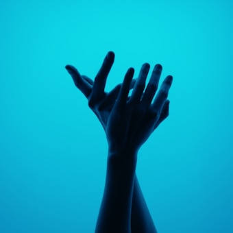 Silhouetted hands elegantly posed against a vibrant turquoise background, creating an artistic and graceful composition.