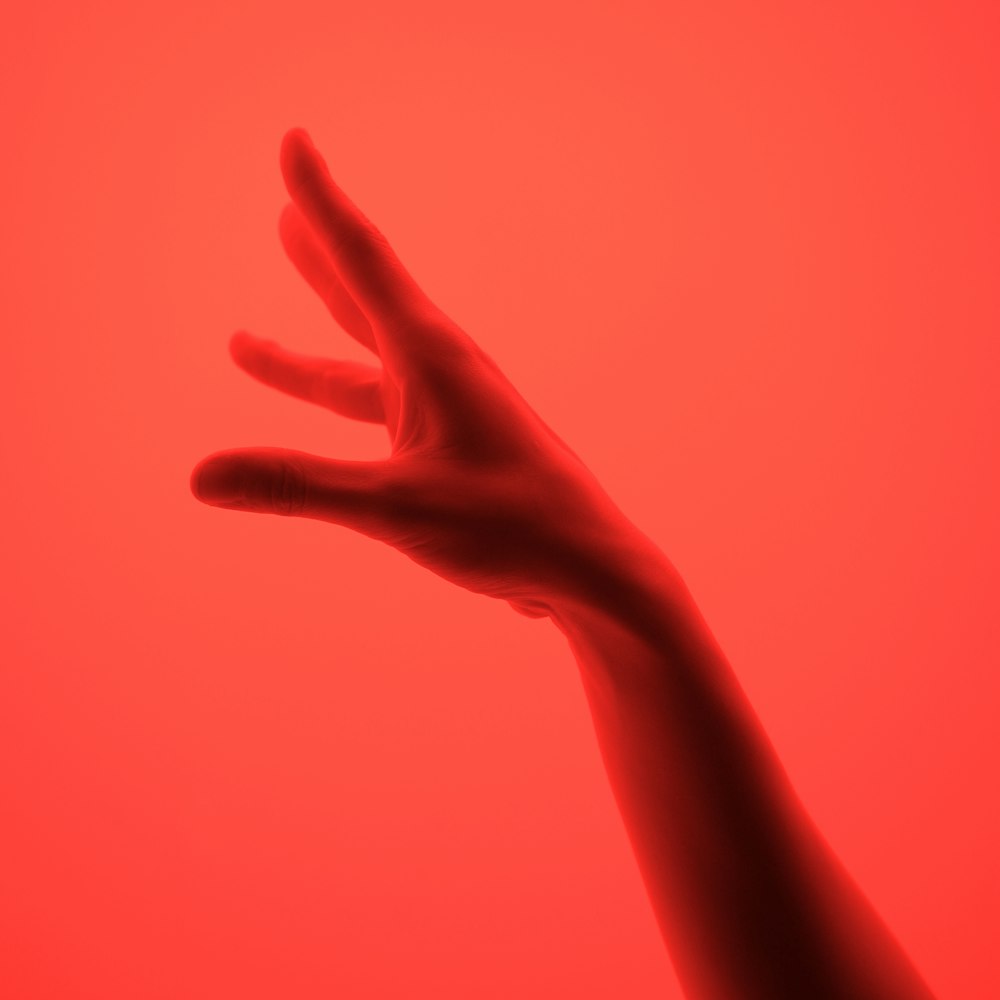 a hand reaching up into the air with a red background