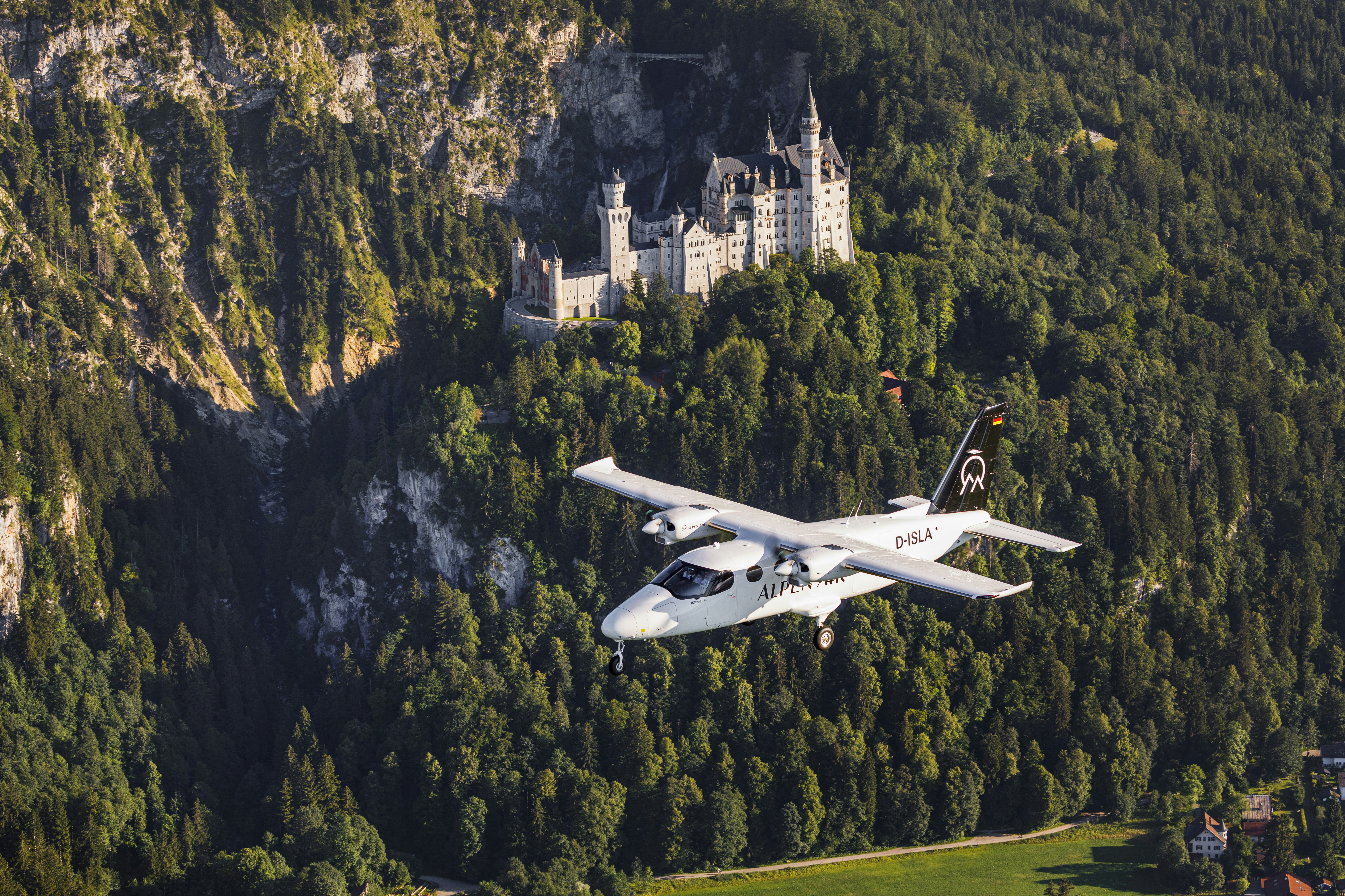 a white plane flying over a lush green forest, A white tecnam plane flying in front of the Neuschwanstein castle in Bavaria, Germany. It is a sunny day and there the landscape in the background consists of the castle, forest, rocks, meadow fields and a mountain.