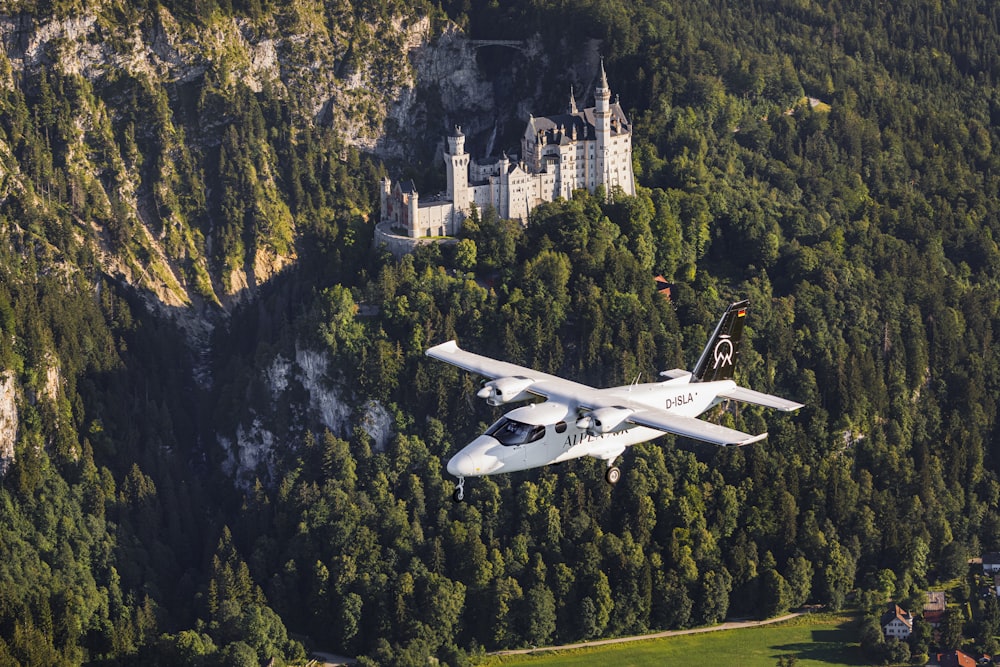 a white plane flying over a lush green forest
