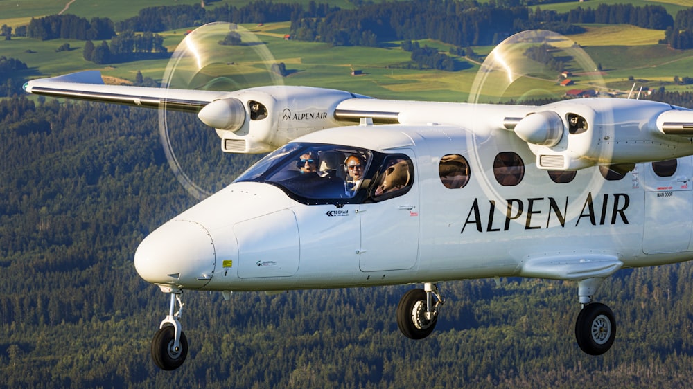 a small airplane flying over a lush green hillside