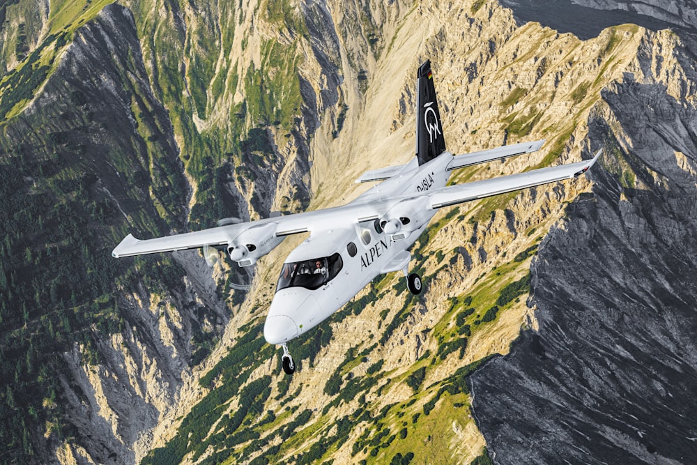 a white airplane flying over a mountain range