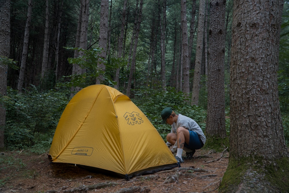 a man kneeling down next to a yellow tent