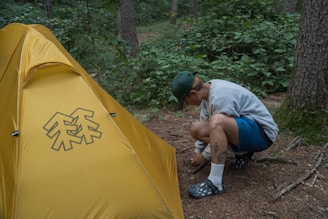 a man kneeling down next to a yellow tent