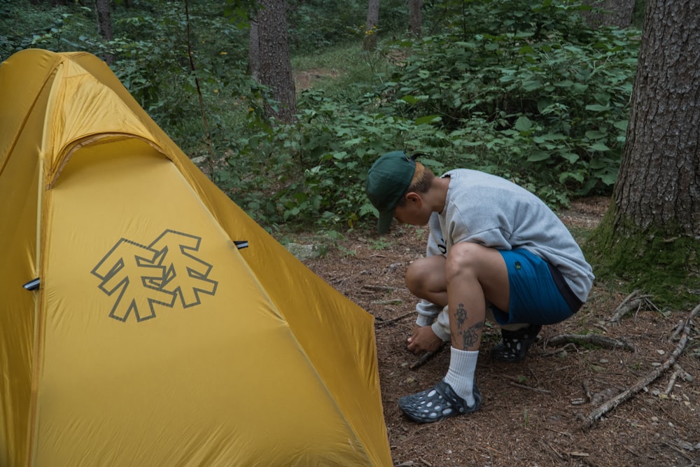 a man kneeling down next to a yellow tent