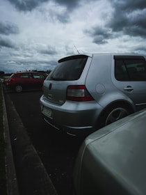 Side view of a silver sedan with visible hail dents before repair, parked under a cloudy sky.