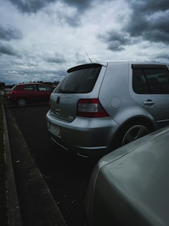 Side view of a silver sedan with visible hail dents before repair, parked under a cloudy sky.