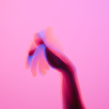 An abstract image features a hand with a motion blur effect against a pink background. The hand appears to have a double exposure effect with blue and red hues.