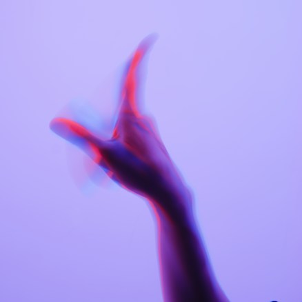 A blurred hand in motion against a light purple background. The hand appears to have a split color effect with shades of red and blue.
