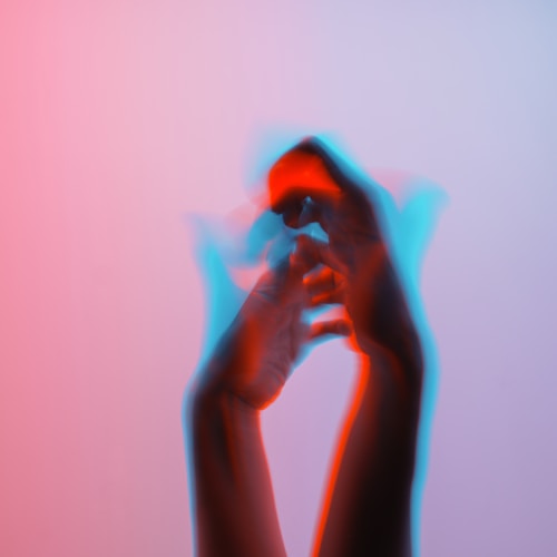 A pair of hands in motion with a motion blur effect, creating a dynamic and artistic visual. The hands appear to be set against a gradient background with hues of pink and light blue, giving a sense of fluidity and expression.
