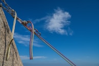 Several climbing ropes and carabiners are securely attached to a rock against a clear blue sky with a few white clouds.