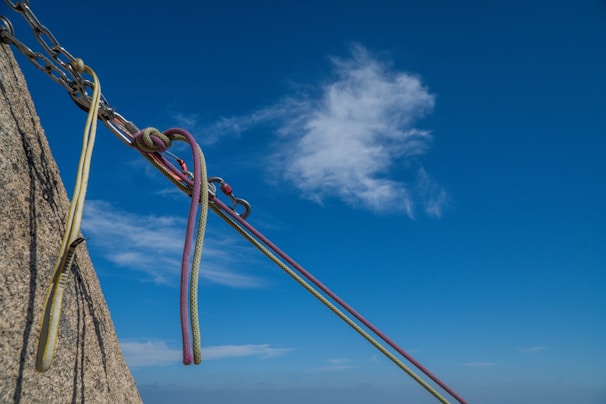 A small group of climbers carefully practicing anchor building on a sunlit natural rock face.