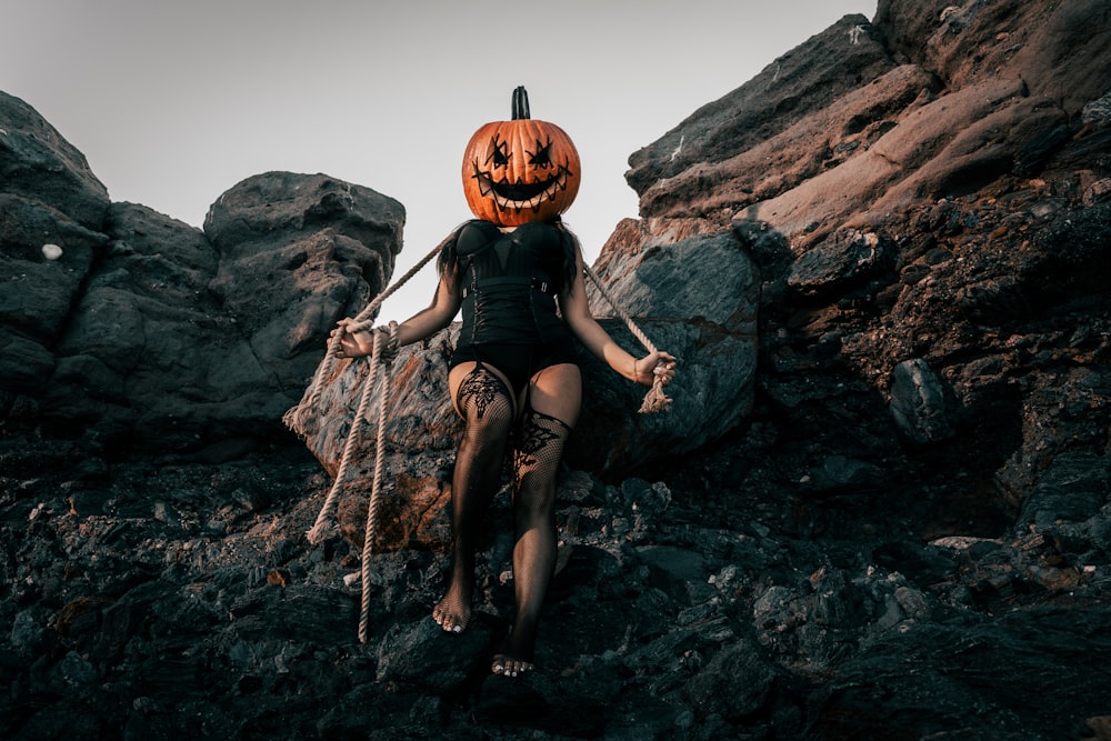 a woman sitting on a rock with a jack - o - lantern on her head
