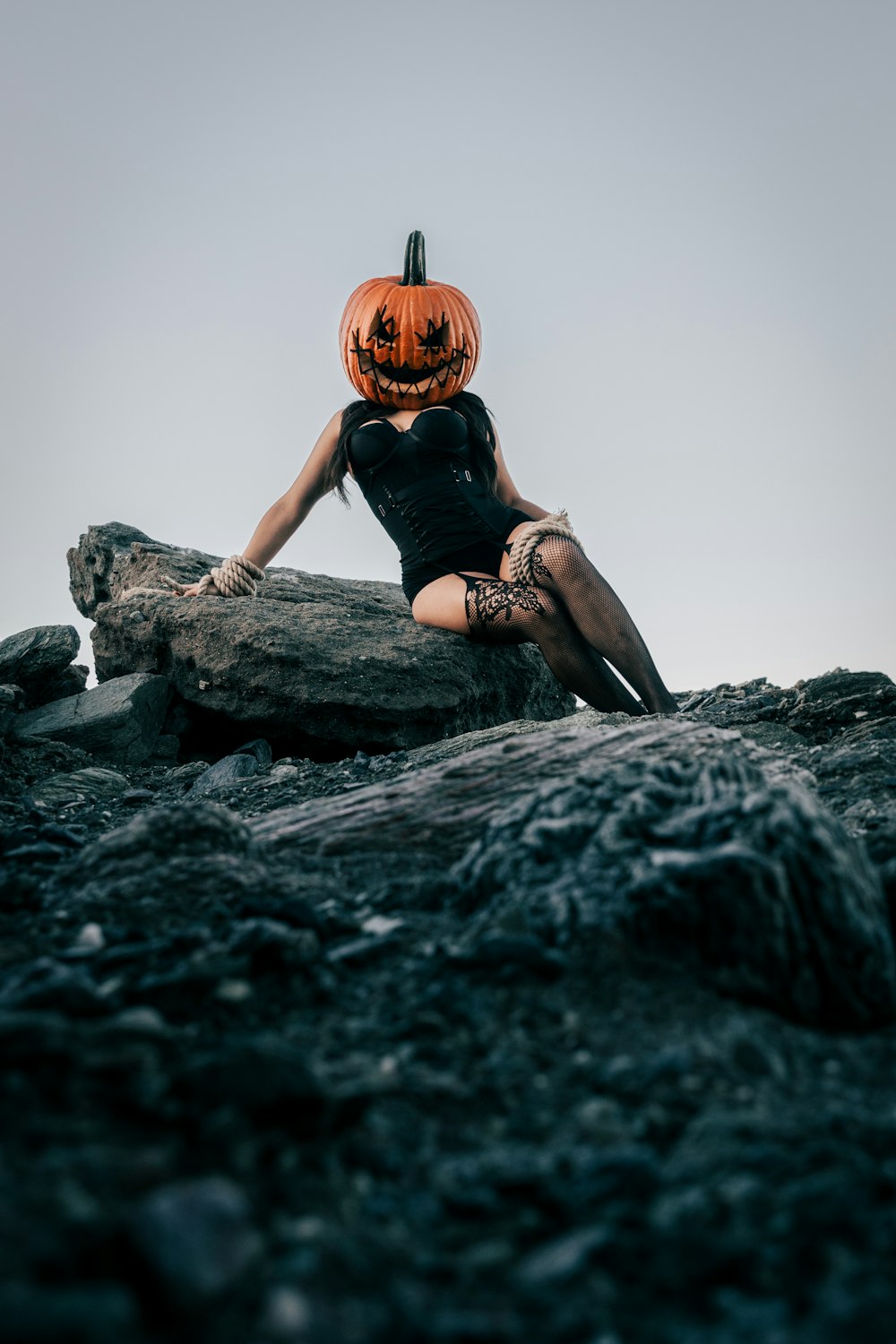 a woman sitting on a rock with a pumpkin on her head