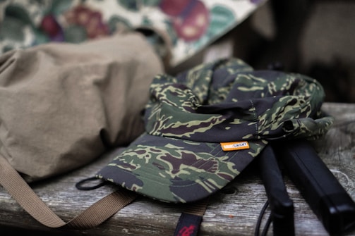 Close-up of camo-patterned gear resting on a mossy log in the woods.