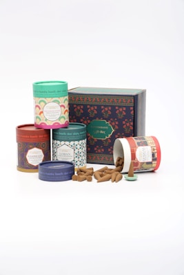 Assorted incense cones are displayed alongside colorful cylindrical packaging with intricate designs. A larger box labeled as a gift box is positioned behind the containers, adding a decorative and festive element.