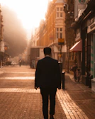 Model wearing a tailored suit walking through a sunlit cobblestone street.