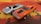 Two toy cars are positioned on a surface with a bright pattern. One is a sleek silver sports car with a convertible design, while the other is an orange muscle car featuring black stripes and chrome details. Both cars have a well-defined, glossy finish.