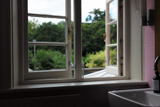 Natural light streaming onto a white marble sink with a small vase of fresh eucalyptus branches.