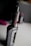 A close-up image of a vaping device with a metal tank and a sleek design. The surface is glossy and metallic, with visible screw details. A blurred background suggests an indoor setting with dim lighting.