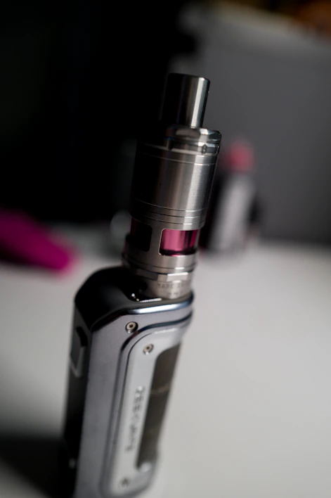 Close-up of a sleek vape pen with a glowing tip resting on a wooden table.