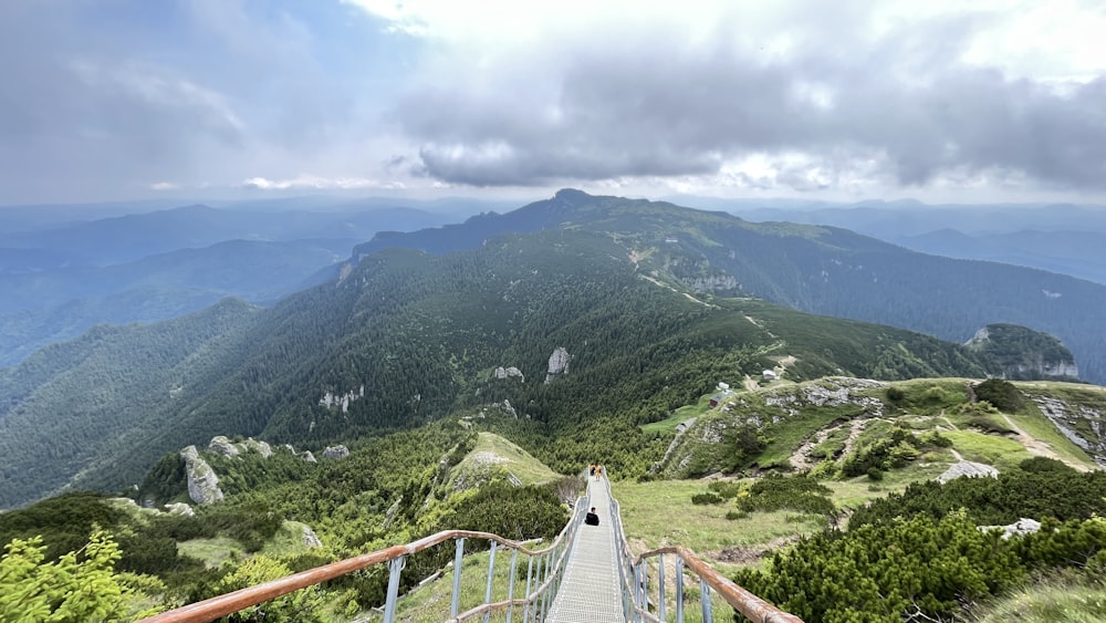 a wooden walkway going up a hill with mountains in the background