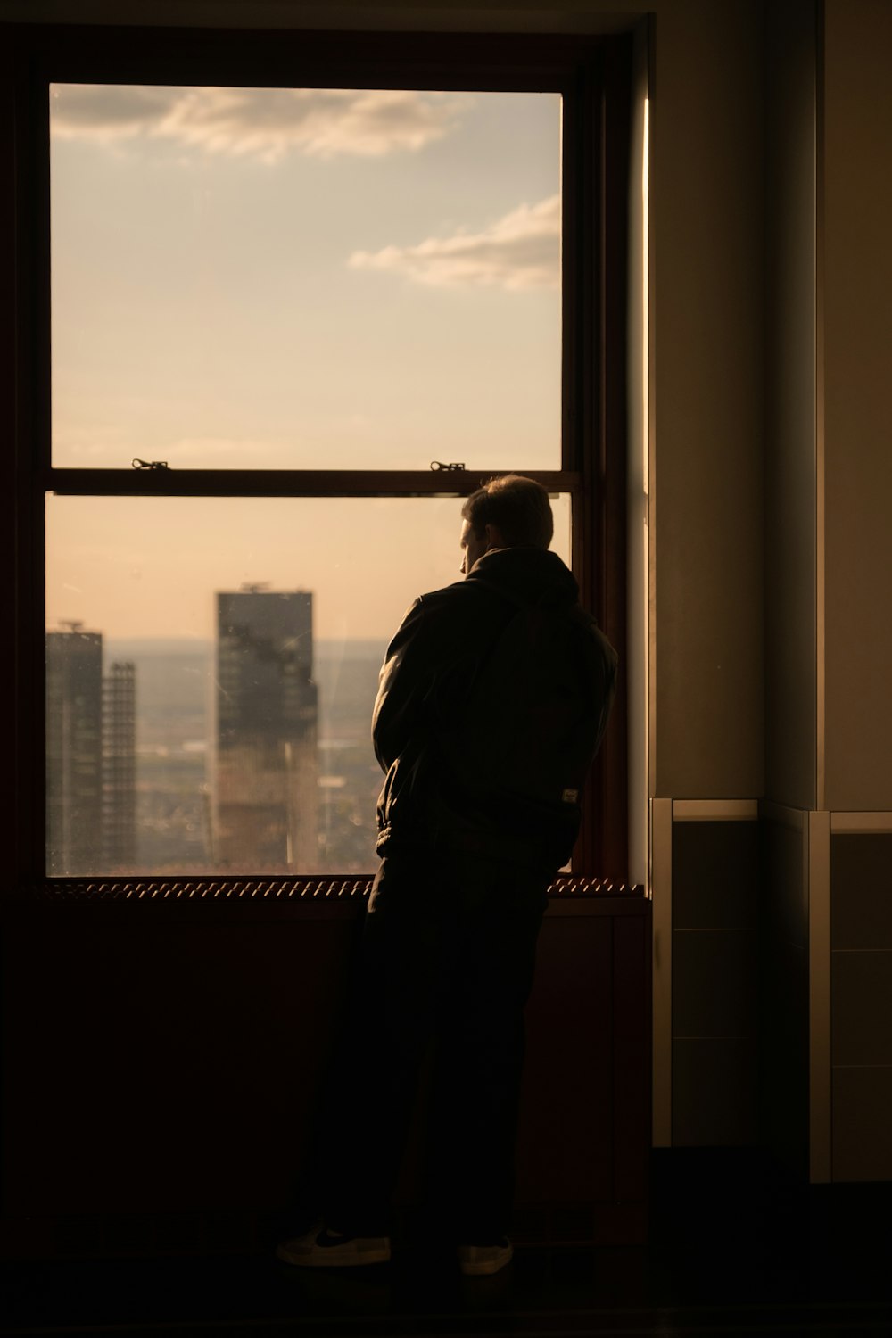 a man standing in front of a window looking out at the city