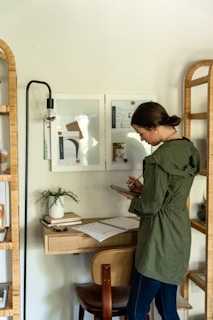 A person reading a digital tablet while sitting at a cozy desk surrounded by books and a plant.