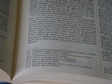 An open book displaying a page with text in columns. The text appears to be from a religious or historical document, likely a Bible, with passages numbered and explanations or annotations at the bottom of the page.