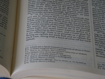 An open book displaying a page with text in columns. The text appears to be from a religious or historical document, likely a Bible, with passages numbered and explanations or annotations at the bottom of the page.