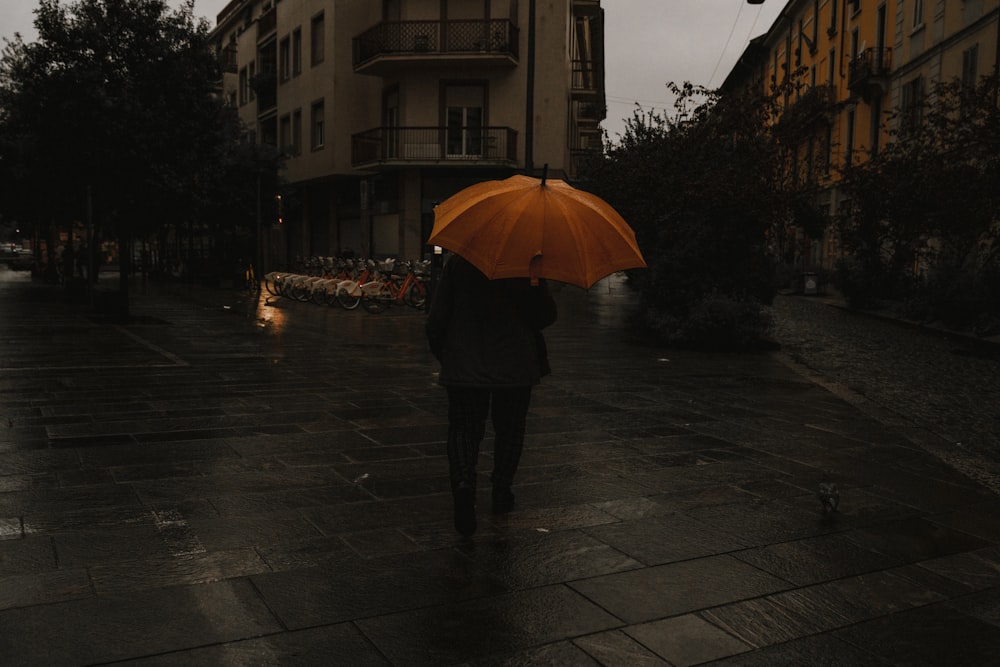 a person walking down a street holding an orange umbrella