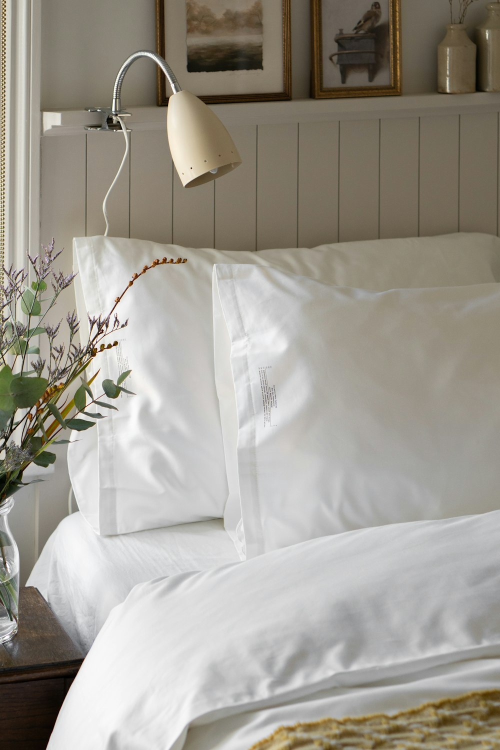 a bed with white sheets and pillows and a vase with flowers