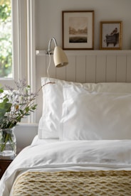 Bedding, pillows, a lamp, and a plant in a vase
