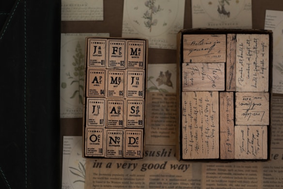 A vintage-style display with a calendar and blocks featuring handwriting. The calendar includes sections for each month with names and numbers. The blocks have various handwritten notes and appear aged. In the background, there are botanical illustrations and pages with text, creating an antique ambiance.