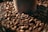 A close-up view of a pile of roasted coffee beans surrounding the base of a brown coffee cup. The beans have a shiny surface and rich, dark brown color, suggesting freshness and a roasted aroma.
