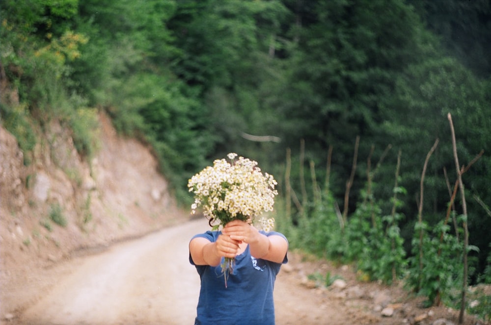 a person holding a bunch of flowers on a dirt road