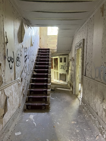 A dimly lit empty hallway with peeling wallpaper.