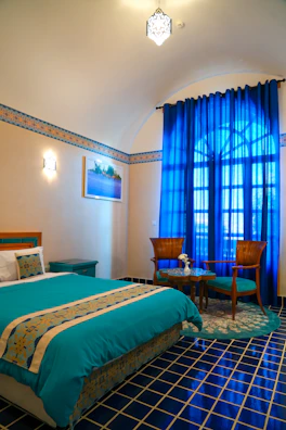 A luxurious bedroom with cream beige bedding and navy blue curtains softly lit by turquoise lamps.