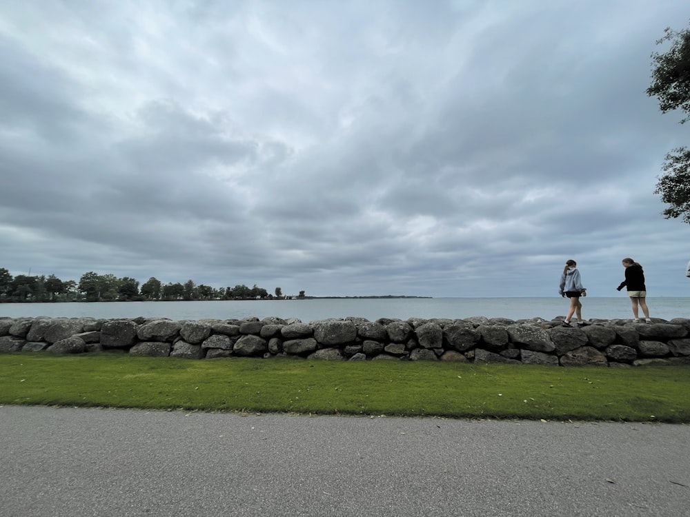 a couple of people standing next to a stone wall